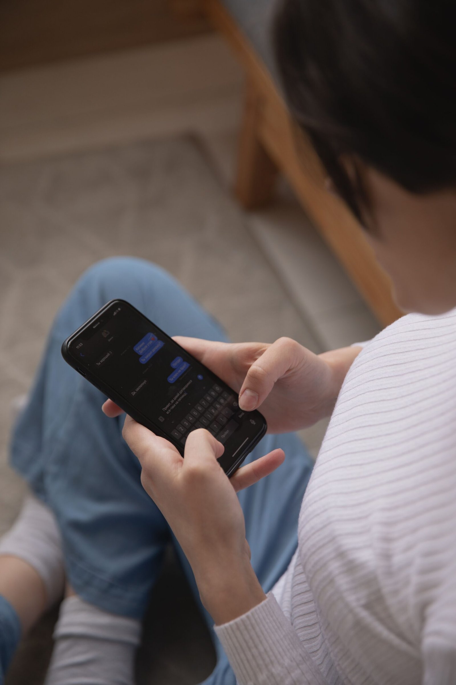 Person sitting indoors and using a smartphone to send a message.
