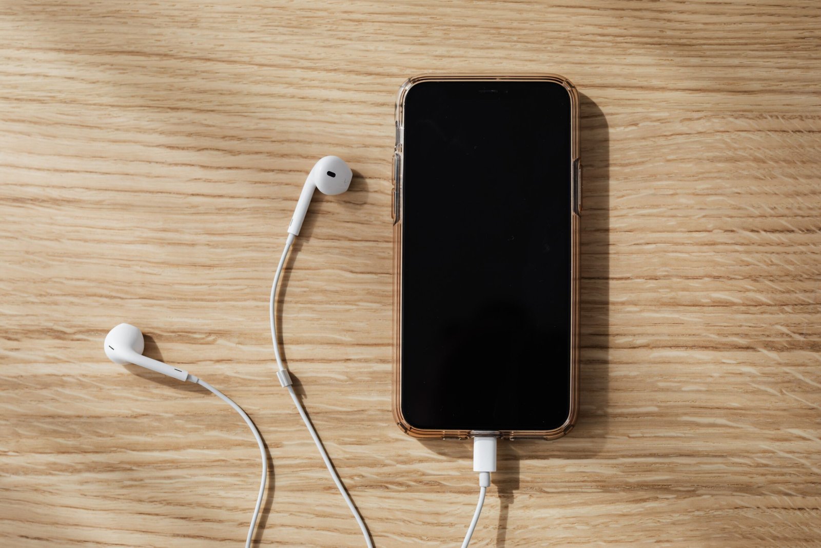 Smartphone with wired earphones resting on a wooden table, with the phone screen turned off.